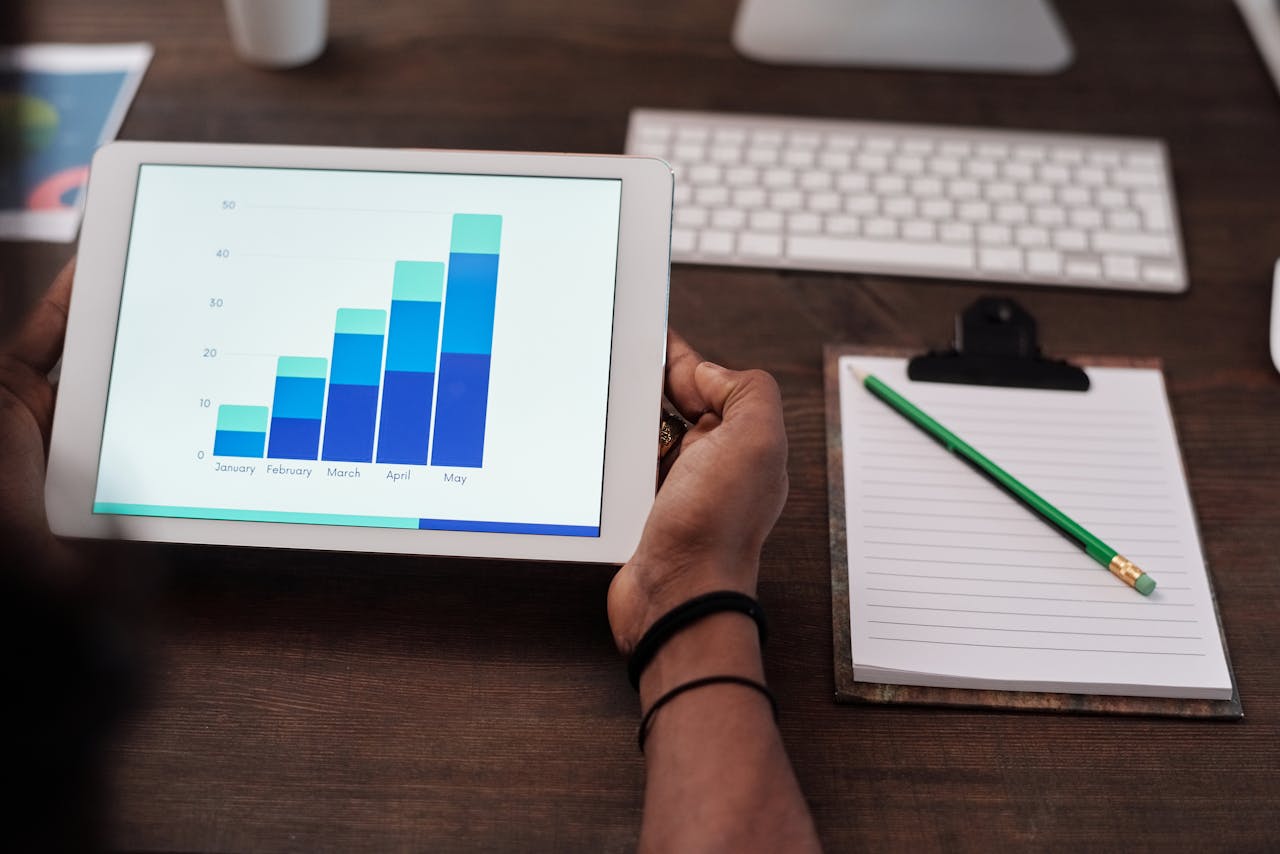 Home Close-up of a person holding a tablet showing growth charts on a wooden desk setup.
